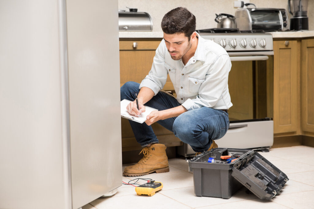 portrait handsome male technician doing work report broken fridge home kitchen
